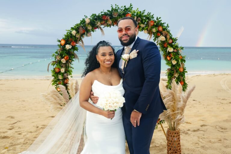 Bride and groom under a floral arch on the beach at their destination wedding — photographed by 121 Media Group