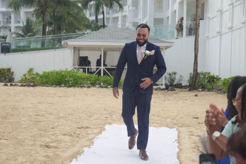 Groom walking down a white beach aisle before the ceremony — photographed by 121 Media Group