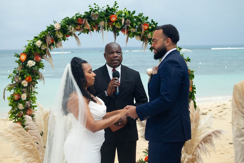 Bride and groom exchanging vows under a floral arch by the ocean — photographed by 121 Media Group