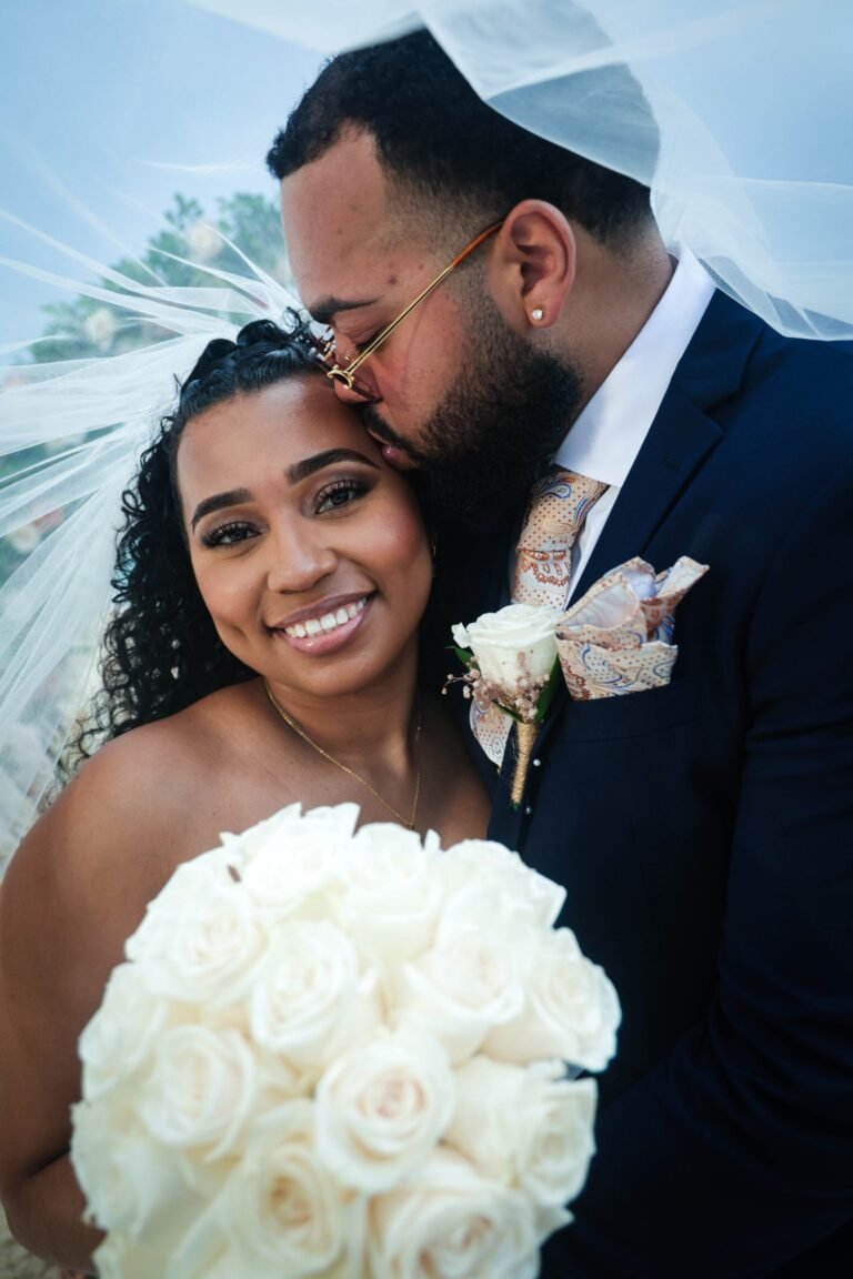 Groom kissing the bride's forehead, close portrait with bouquet — photographed by 121 Media Group