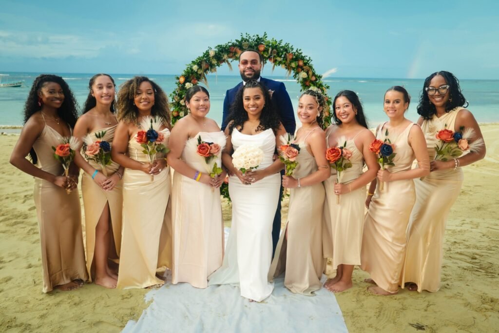 Bride with her bridesmaids under the floral arch on the beach — photographed by 121 Media Group