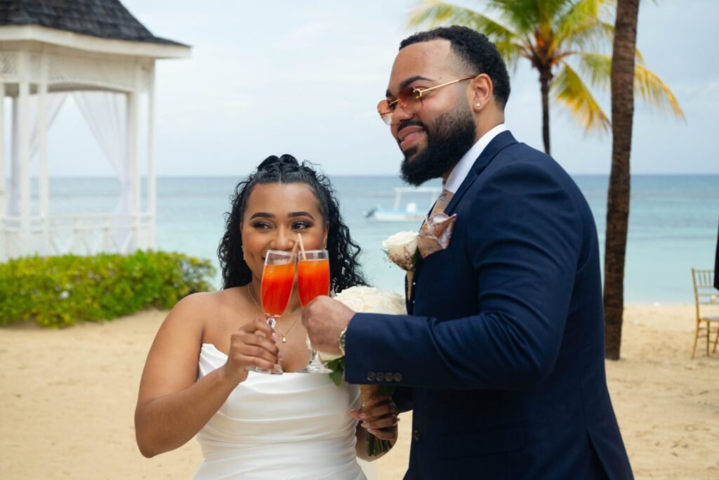 Bride and groom toasting with drinks on the beach — photographed by 121 Media Group