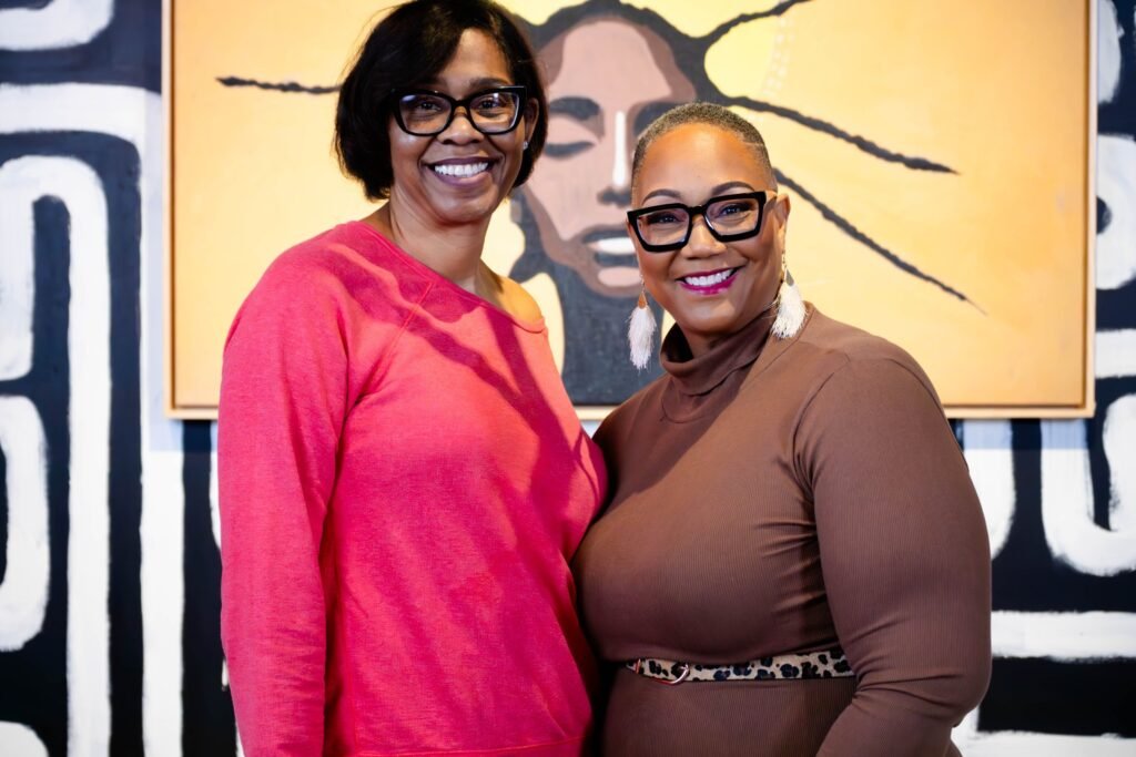 Two podcast guests posing together in front of a sunburst portrait mural — photographed by 121 Media Group